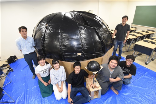 プラネタリウムドームの前で記念撮影するプロジェクトメンバー＝福井大の文京キャンパス